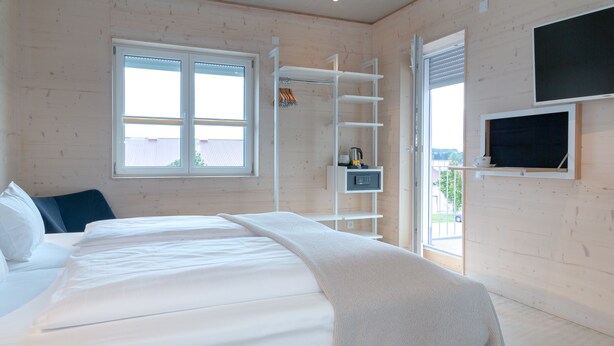 A bedroom with a bed, a TV, a window, and a shelf with items. - Schlafzimmer Hotel (Dinkelsbuehl)