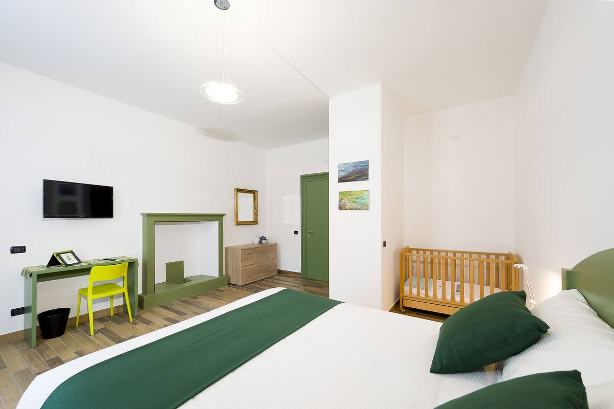 Une chambre à coucher comprenant un lit, un bureau, une chaise, un berceau et un téléviseur.