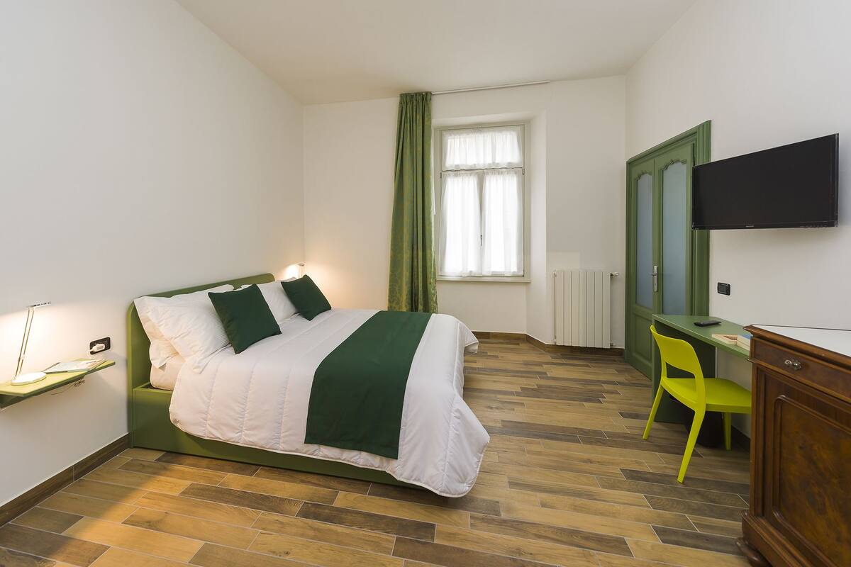 Une chambre d’hôtel équipée d’un lit, d’un bureau, d’une chaise, d’une télévision et d’une fenêtre avec des rideaux.