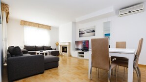 Una sala de estar moderna con un sofá, una mesa de comedor con sillas, un televisor de pantalla plana y una chimenea.