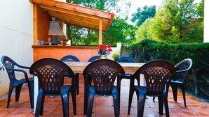 Un patio al aire libre con una mesa y sillas de madera, un horno de ladrillo y un jarrón con flores.