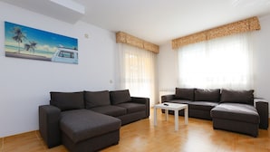 Una sala de estar con dos sofás oscuros, una mesita blanca y un cuadro que muestra una playa.