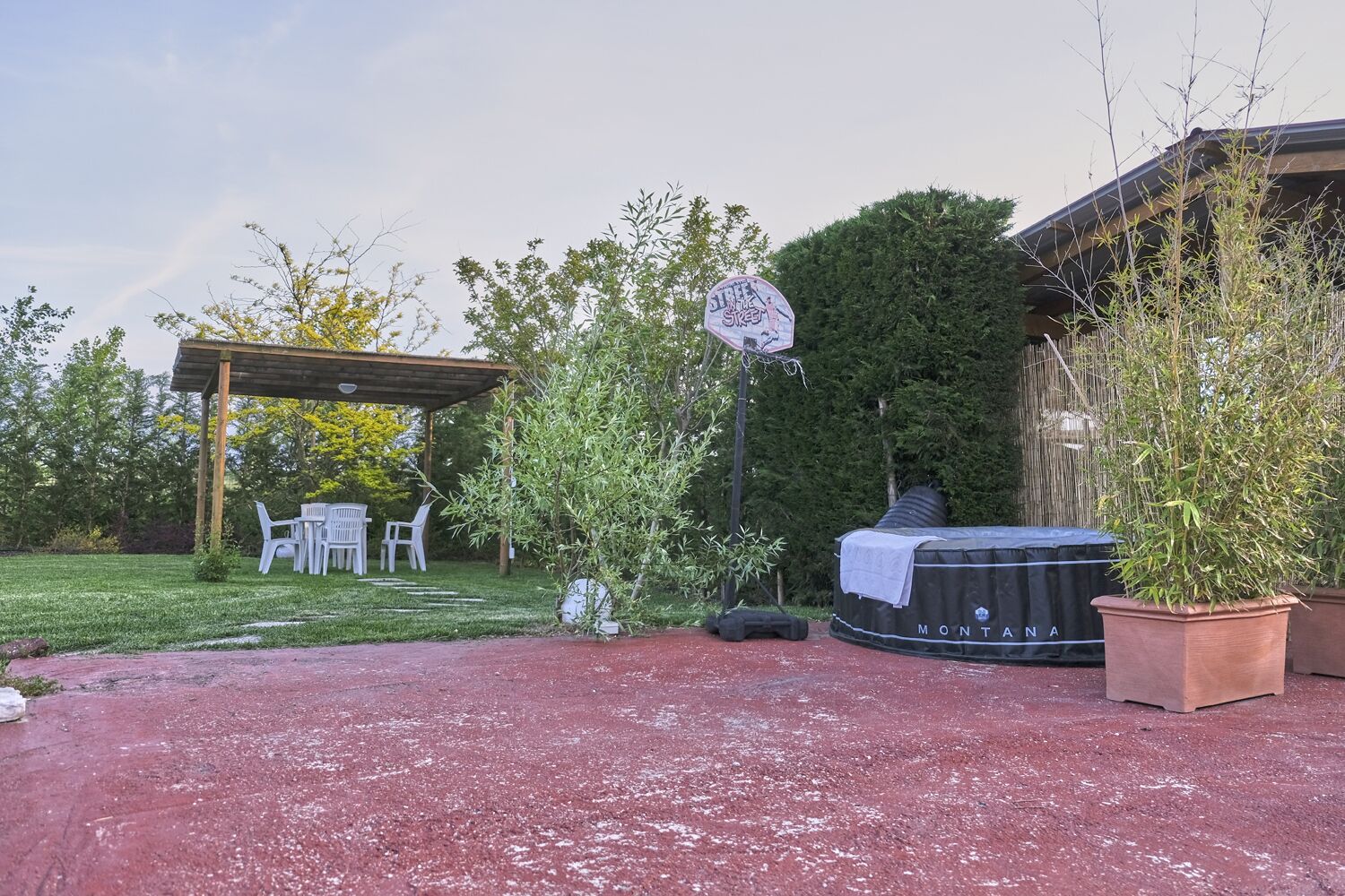 Een overdekt terras met buitenmeubilair, een jacuzzi en potplanten.