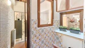 Un couloir étroit aux murs recouverts de carreaux décoratifs, une porte en bois et une fenêtre ornée de plantes en pot.