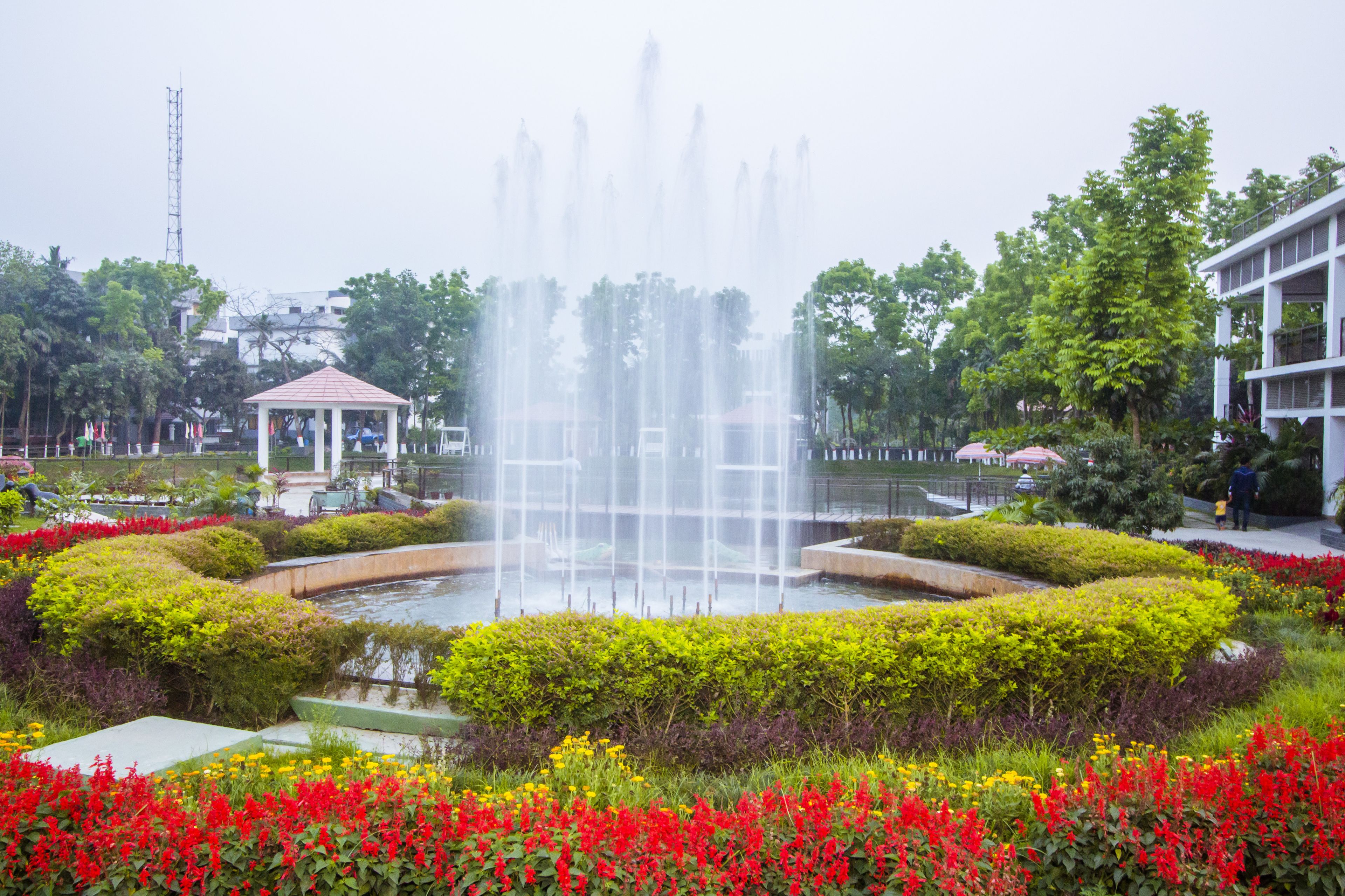 A garden with a central fountain, surrounded by well-maintained hedges and colorful flower beds.