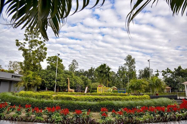 A landscaped garden with a giraffe statue, palm trees, and red flowers.