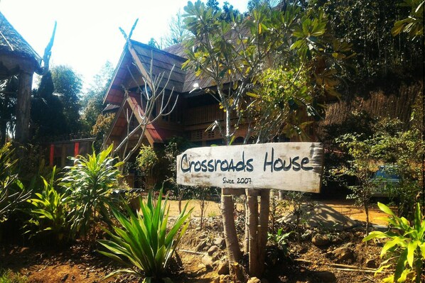 Un letrero de madera que indica Crossroads House, con una casa rústica al fondo.