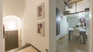 Un couloir avec un escalier, un coin repas avec des chaises et une table, et deux tableaux encadrés accrochés au mur.