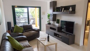 A living room with a brown leather sofa, a white coffee table, a flat-screen TV on a dark wooden stand, and a small plant on a shelf. - Villa Leonard in Playa Blanca (Playa Blanca)