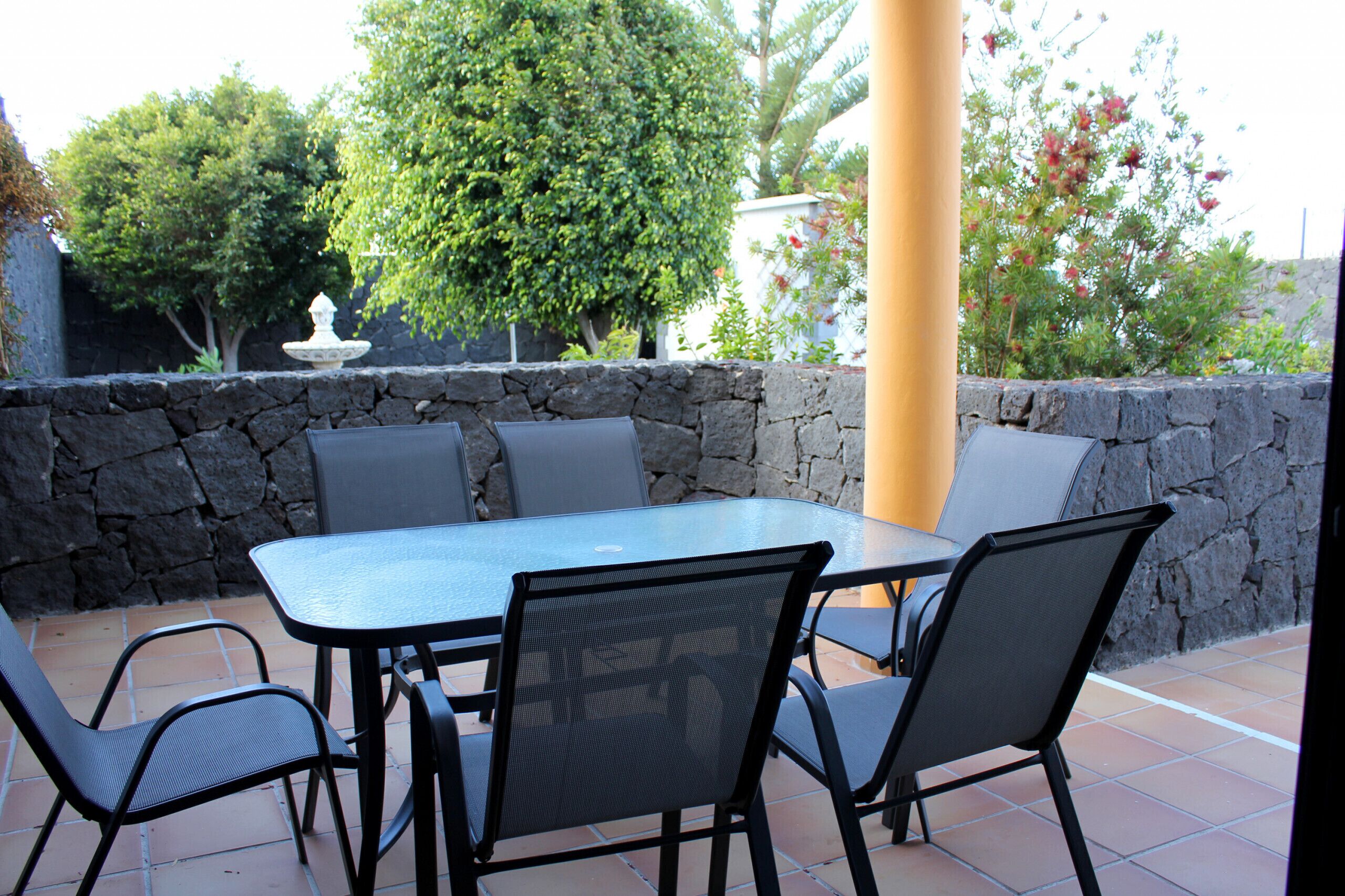 Un patio al aire libre con una pared de piedra, una mesa redonda y cuatro sillas.