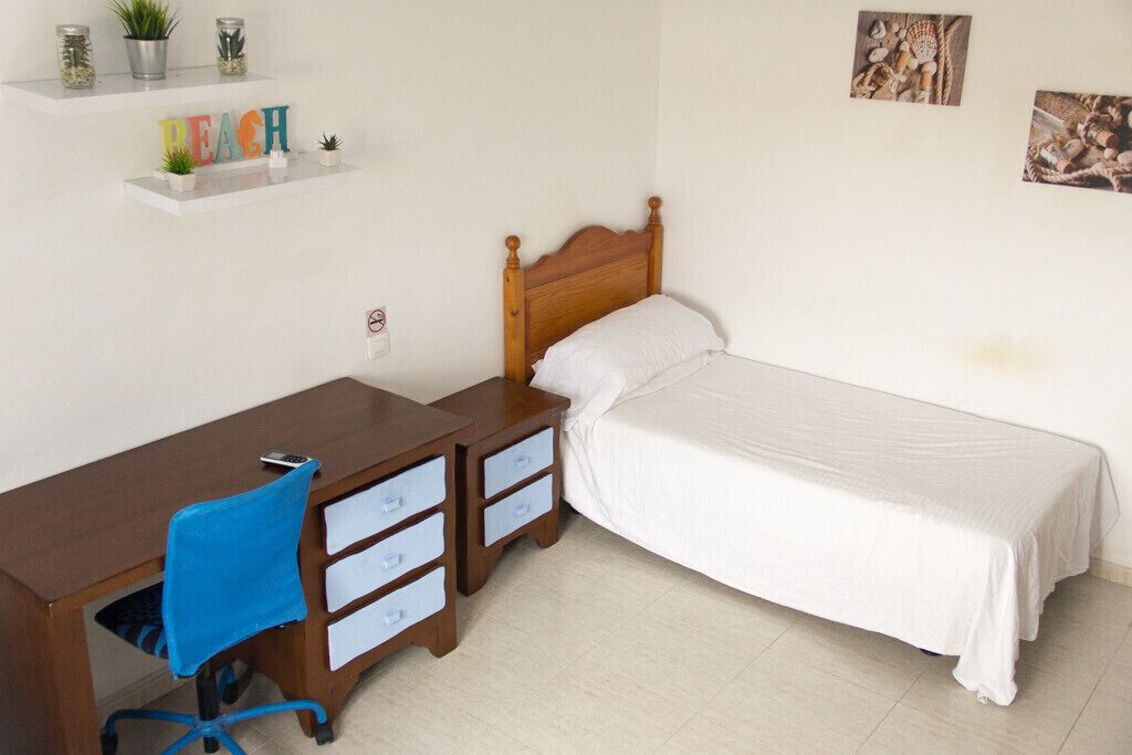 A bedroom with a wooden bed, a desk with drawers, a chair, and shelves with decorative items.