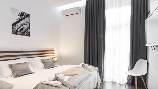 A modern hotel room with a large bed, a flat-screen TV, a desk, and a window with curtains.