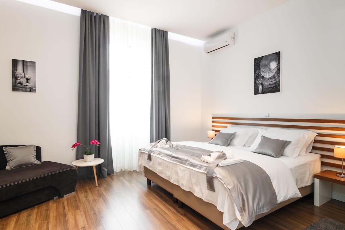 A modern bedroom with a large bed, a bedside table, a small sofa, and a window with curtains.