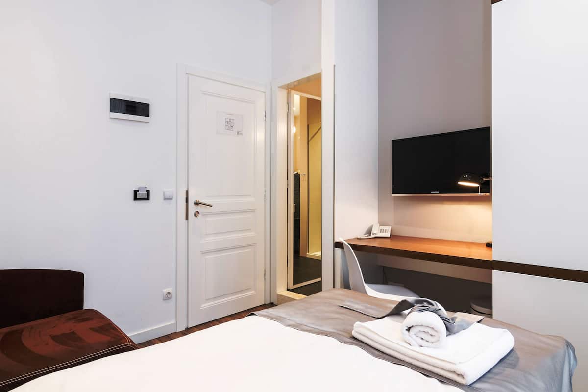 A hotel room with a bed, a desk, a chair, a TV, and a door.