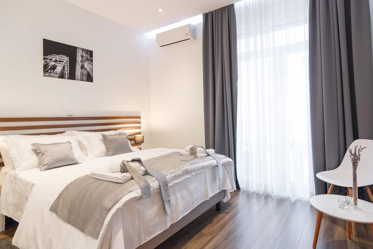 A hotel room with a bed, a bedside table, a chair, and a large window with curtains.