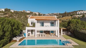 Una casa de dues plantes amb piscina, espai d'estar a l'exterior i vistes als turons circumdants.