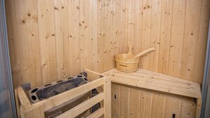 Sauna de fusta amb una panxa, un cubell i un tamboret de fusta.