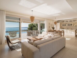 Een ruime woonkamer met een grote bank, een eettafel en uitzicht op zee door grote ramen.