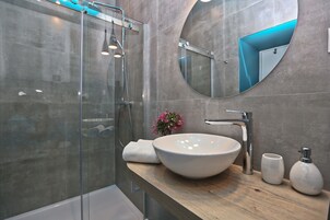 A modern bathroom with a glass-enclosed shower, a large round mirror, and a wooden vanity with a white vessel sink.