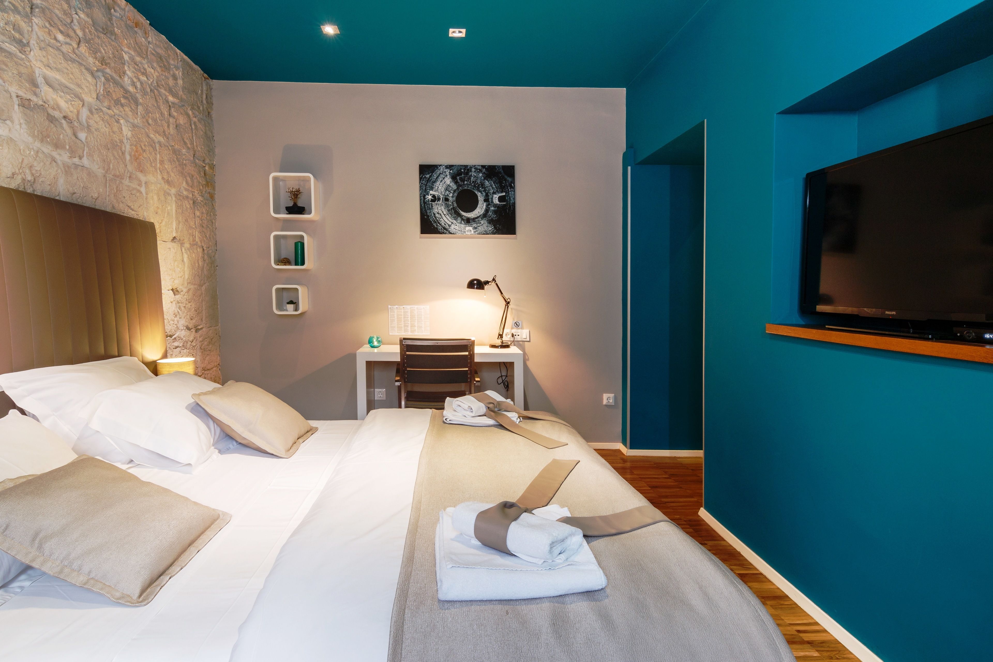 Een moderne hotelkamer met een groot bed, een bureau, een flatscreen televisie en een wand met stenen details.