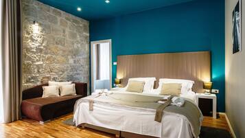 Un dormitorio moderno con pared de piedra decorativa, una cama grande con cabecera de madera, un sofá marrón y una mesita de noche con lámpara.