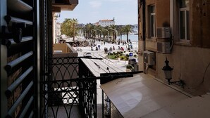 A balcony with a metal railing overlooking a busy street with pedestrians and vehicles.