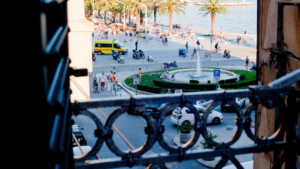 A busy public square with palm trees, a fountain, and a view of the sea.