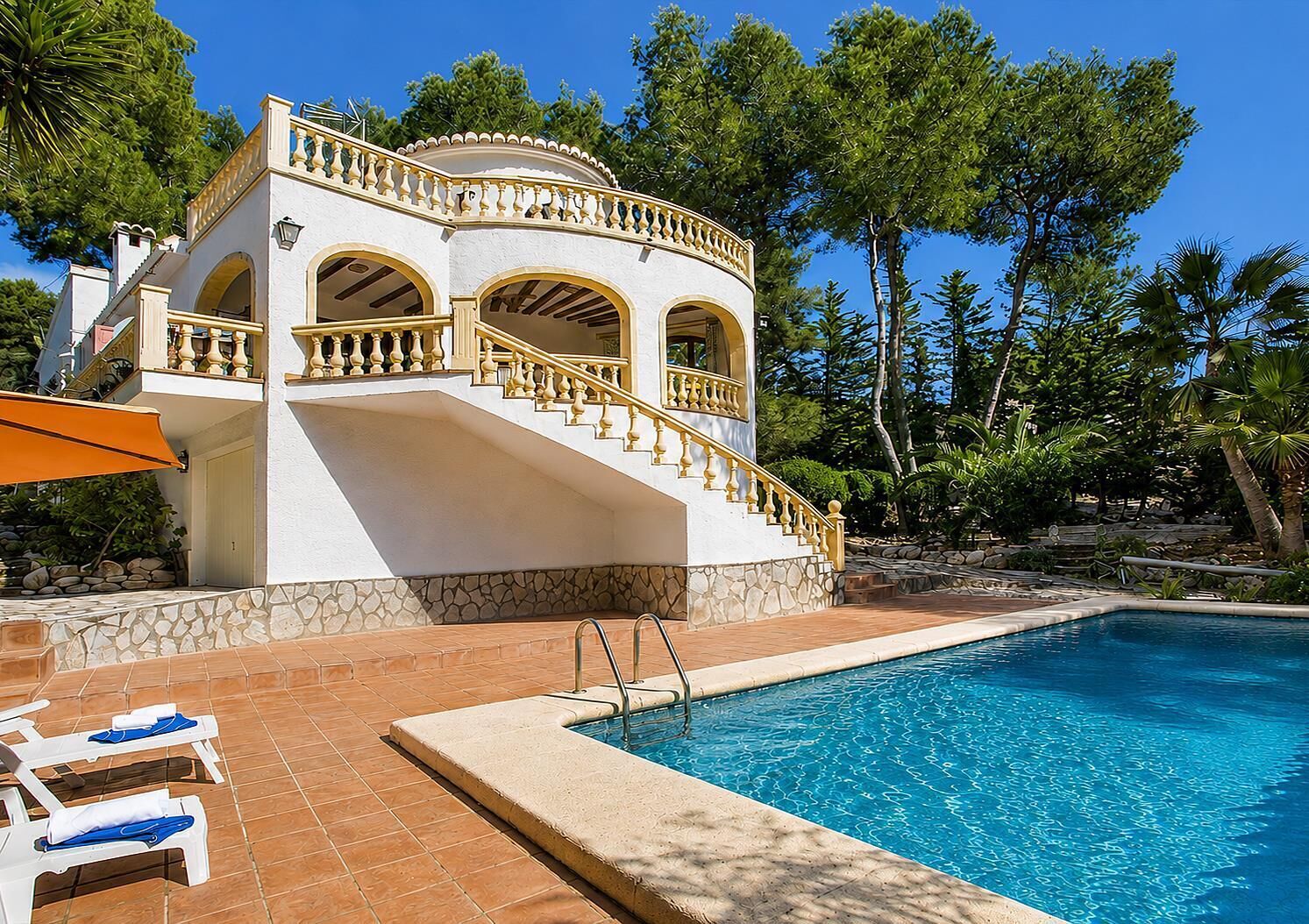 A poolside view of a building with a stone facade, a staircase with balustrades, and a clear blue pool.