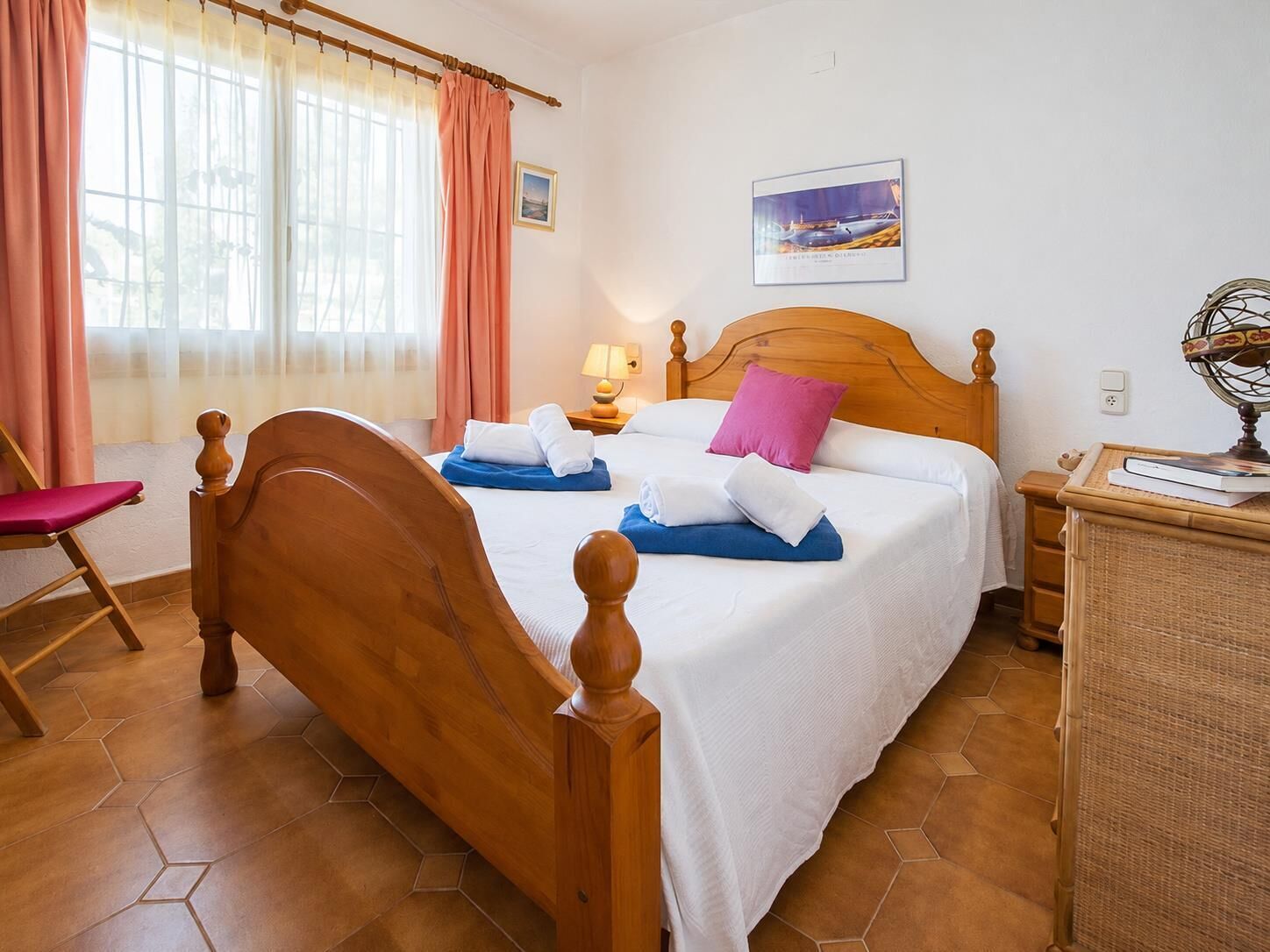 A neatly arranged bedroom with a wooden bed, a chair, a bedside table with a lamp, and a wall-mounted globe.