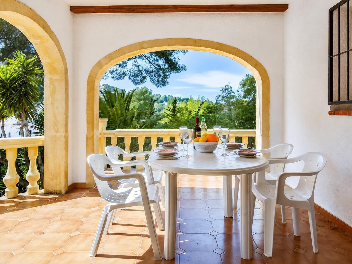 A round table with chairs, a view of greenery, and a bottle on the table.