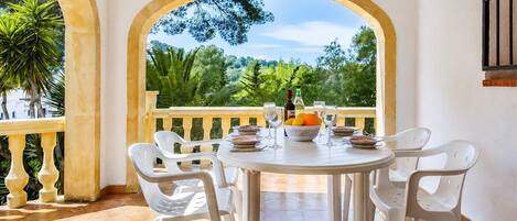 A round table with chairs, a view of greenery, and a bottle on the table.