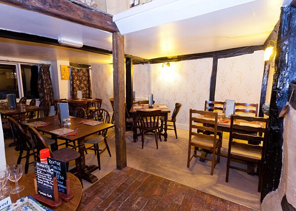 A cozy restaurant with wooden tables and chairs, a chalkboard menu, and a brick floor.