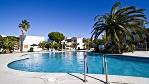 Una piscina de borde curvo, rodeada de palmeras y edificios con balcones.