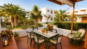 Un patio con mesa y sillas, rodeado de follaje y edificios.