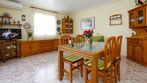 Un comedor con una mesa de vidrio, sillas de madera y un televisor sobre un mueble.