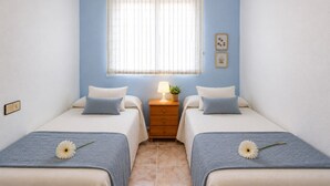 Un dormitorio con dos camas, una mesita de noche con lámpara, una ventana con persianas y una pequeña decoración en la pared.