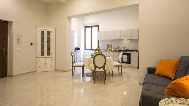 Un'ampia zona giorno con tavolo da pranzo, sedie, divano e cucina sullo sfondo.