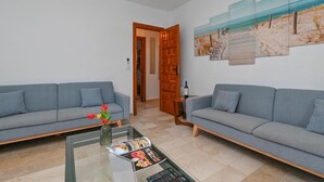 A living room with two grey sofas, a glass coffee table with magazines, and a door leading to another room. - Escabusso 6 pax - Javea, Costa Blanca (Javea)