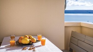 Ein Tisch mit Früchten und Orangetassen auf einem Balkon mit Blick auf ein Gewässer.