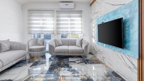 A modern living room with two grey sofas, a large TV mounted on a marble wall, and a ceiling air conditioner. - Awesome home in Fazana (Fazana)