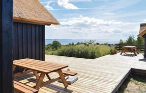 Een houten terras met een picknicktafel en een constructie met rieten dak.