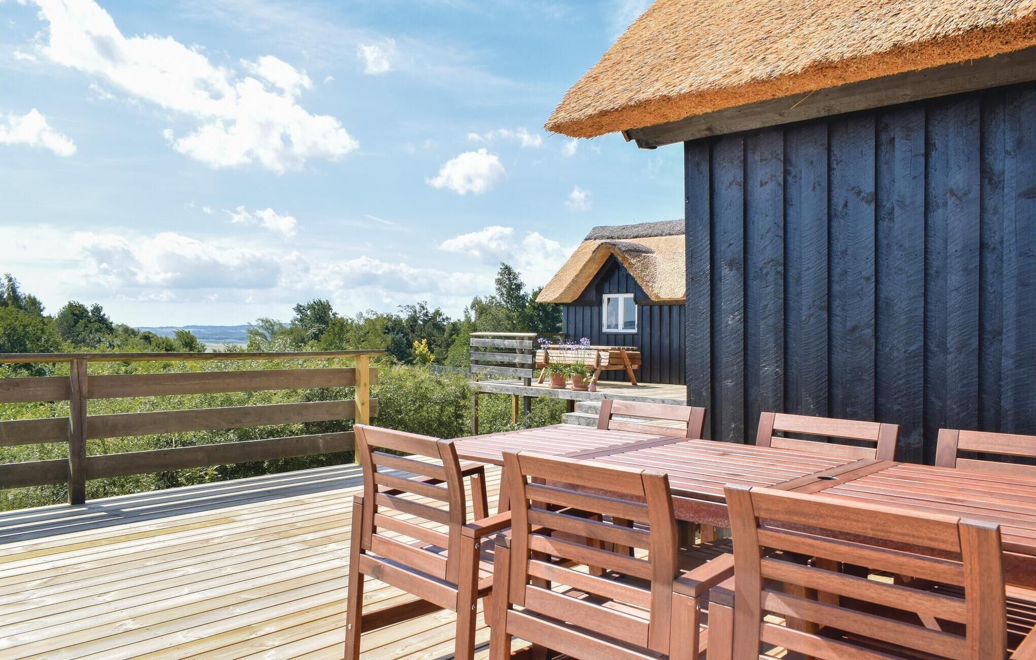Une terrasse en bois avec un bâtiment à toit de chaume, des meubles en bois et une vue sur le paysage.