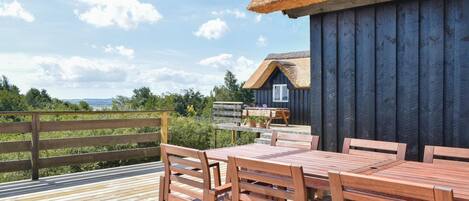 Une terrasse en bois avec un bâtiment à toit de chaume, des meubles en bois et une vue sur le paysage.