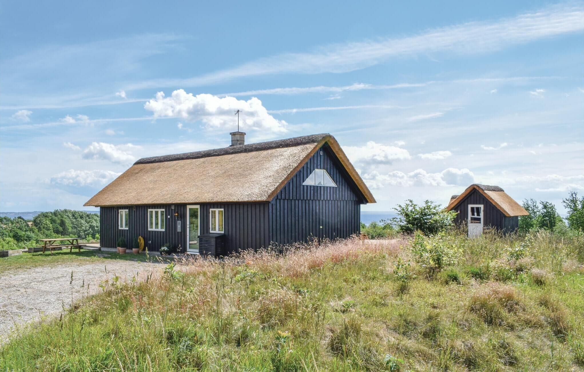 Two thatched-roof cottages with wooden walls, a picnic table, and a gravel path.