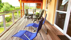 Un espace extérieur aménagé, abrité et doté d’une table et de chaises, d’une terrasse en bois et d’une porte vitrée donnant sur un jardin.
