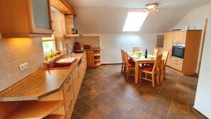 Une cuisine avec des meubles de rangement en bois, une table à manger avec des chaises et un four encastré.