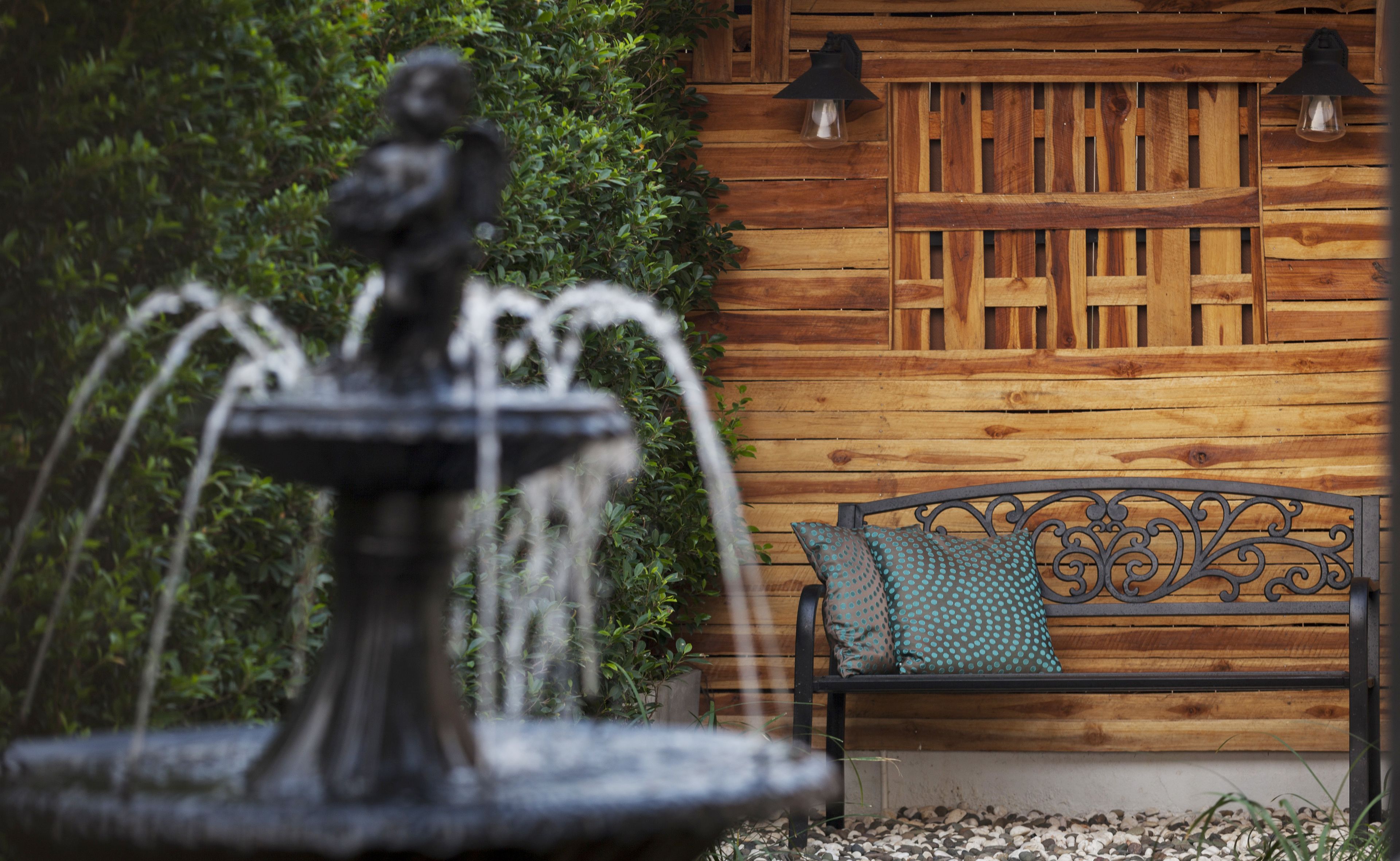 A fountain with water jets in front of a wooden wall with a bench and two wall-mounted lights.
