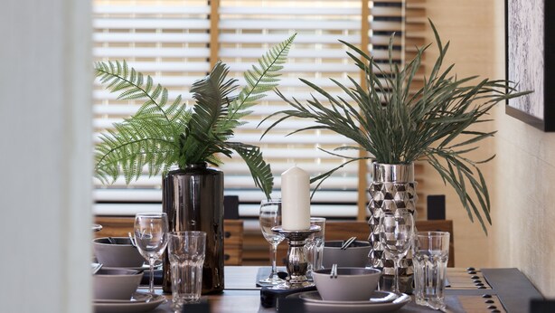 A dining table set with glassware, plates, and decorative vases with plants. - Nan Garden House (Nan)