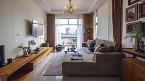A modern living room with a large sofa, a flat-screen TV, wooden furniture, and a chandelier. - Nan Garden House (Nan)