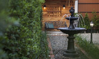 Una fuente con una estatua en un jardín, con un muro de madera y un banco al fondo.